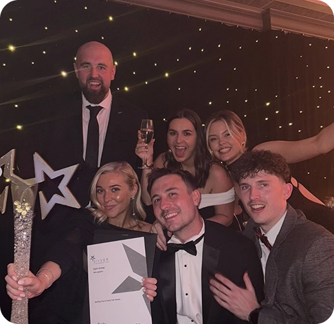 Six colleagues celebrate a silver award at a formal event, holding a star-shaped trophy and certificate beneath warm lights.